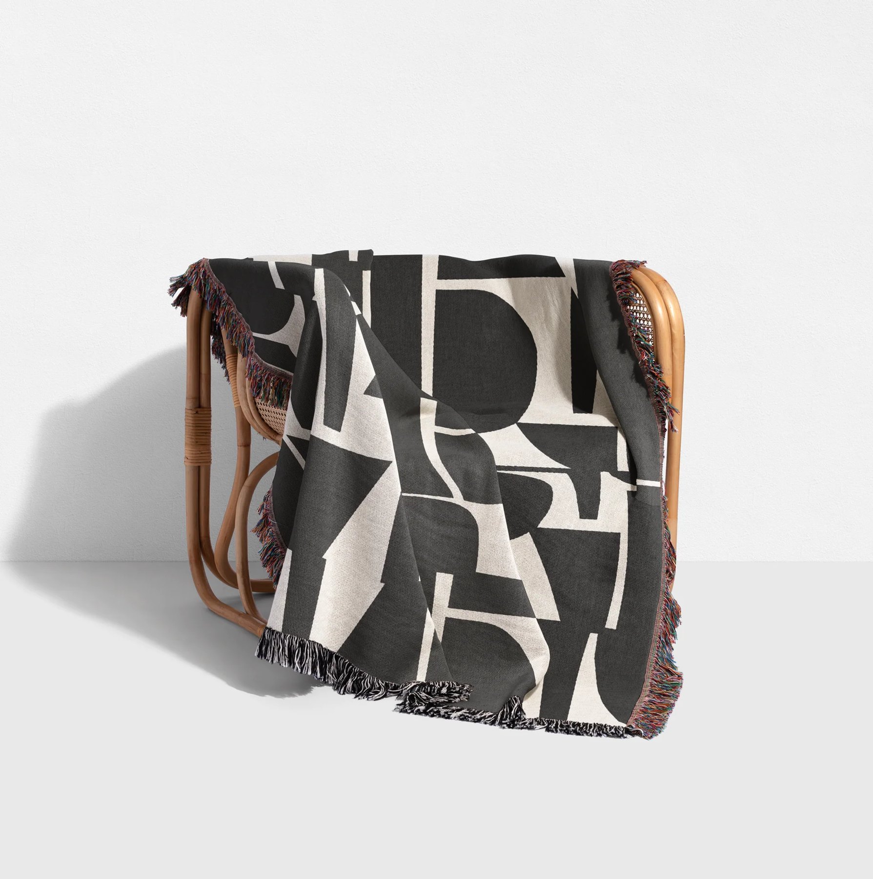 A woven blanket in a bold black and cream geometric pattern draped over a rattan chair