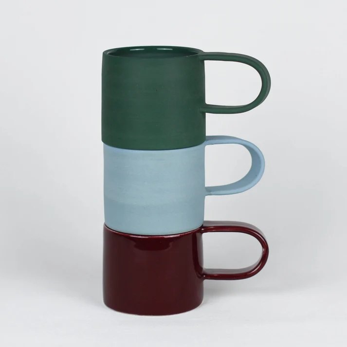Three stoneware mugs stacked, in green, pale blue and oxblood